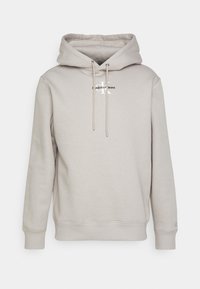 Svetle šedá mikina s kapucí vyrobená z měkké tkaniny. Obsahuje kapuci se šňůrkou, klokankovou kapsu a logo ve středu. Hladké manžety a lem.