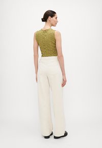 Olive green textured top with a fitted design, paired with off-white wide-leg trousers. Back view shows the top's detailed pattern and waistline.