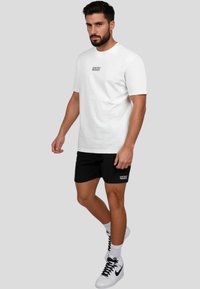 Hvid bomulds T-shirt med teksten "WRONG FRIENDS", parret med sorte shorts med det samme logo. Sorte høj-top sneakers fuldender looket.