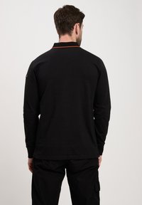 Czarna koszulka polo z długim rękawem i pomarańczowym akcentem na kołnierzyku. Posiada teksturowany materiał, dopasowany krój oraz detal w bocznych szwach.