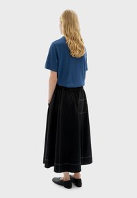 Blauw topje met korte mouwen gecombineerd met een zwarte maxi-rok met zijzakken en contrasterende stiksels. Zwarte instapschoenen maken de look compleet.