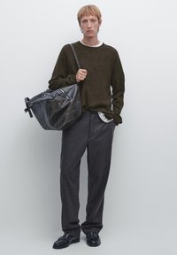 Mørkegrøn strikket sweater, grå stribede bukser, sort lædertaske med sølv detaljer og sorte sko. Ensfarvet baggrund.