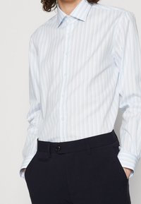 Camisa de algodón a rayas azul claro y blanco con botones. Cuenta con un cuello clásico, mangas largas y un diseño ajustado.