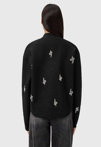 Sort ribbet strikket sweater med sølv slange broderi arrangeret dekorerende over ryggen. Løs pasform med rund halsudskæring.