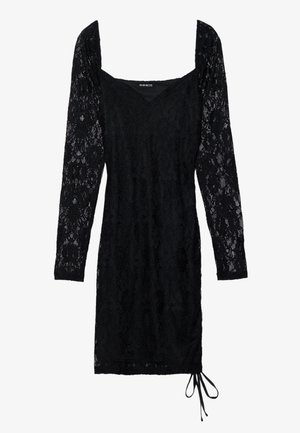 Vestido negro de encaje con mangas largas y transparentes, escote cuadrado y forma ajustada. Presenta un detalle de cordón en el dobladillo.