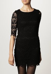 Robe en dentelle noire à manches courtes, avec un ourlet festonné et un motif floral. Le tissu présente un aspect texturé et superposé.