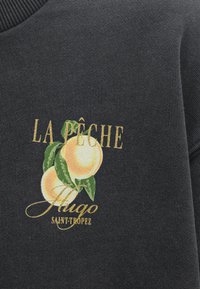 Σκούρο γκρι ύφασμα με τυπωμένο σχέδιο δύο ροδάκινων με πράσινα φύλλα και χρυσό κείμενο που γράφει "LA PÊCHE Hugo SAINT-TROPEZ."