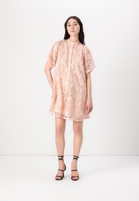 Blonde kjole i myk ferskenfarge med avslappet passform, korte ermer, rund hals og blomsterutskjæringsmønster. Kombinert med svarte sandaler med strapper.