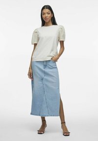 T-shirt di cotone beige con maniche a sbuffo corte e dettagli in pizzo, abbinato a una gonna di jeans azzurro chiaro con spacco frontale e taglio dritto.