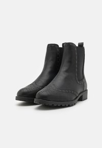 Botas de cuero negro hasta el tobillo con detalles de brogue, paneles laterales elásticos, punta redonda y tacón bajo. Superficie texturizada y acentos decorativos.