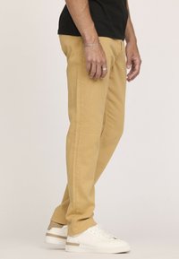 Pantalons slim-fit pour homme en coton jaune moutarde, avec des coutures latérales et une texture subtile, associés à des baskets blanches.