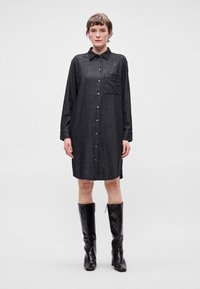 Σκούρα τζιν φόρεμα πουκάμισο με μακριά μανίκια, μπροστινό κλείσιμο με κουμπιά και τσέπη στο στήθος. Συνδυάζεται με μαύρες δερμάτινες μπότες μέχρι το γόνατο.