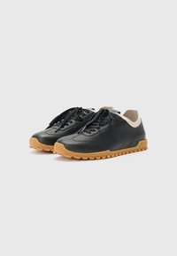 Sneaker in pelle nera con colletto color crema, caratterizzati da una suola di gomma testurizzata color marrone e lacci neri, progettati per l'uso quotidiano.
