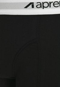Schwarze Leggings aus dehnbarem Stoff. Mit einem weißen elastischen Bund, auf dem "apré" in Schwarz gedruckt ist. Glatte Textur und figurbetontes Design.