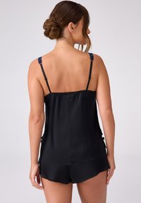 Czarny satynowy zestaw do spania składający się z koszulki na ramiączkach z regulowanymi paskami oraz ozdobnymi kwiecistymi akcentami, w komplecie z pasującymi szortami. Gładka tekstura.