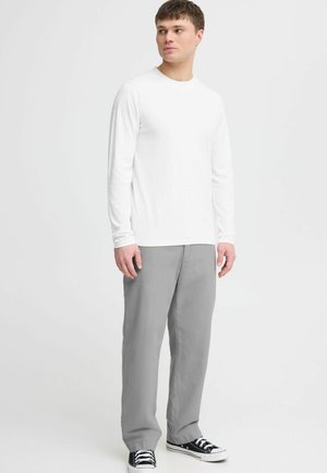 Witte lange mouwen t-shirt, grijze broek, en zwarte sneakers. Glad materiaal, ronde hals, relaxte pasvorm, en zijnaad zichtbaar op de broek.