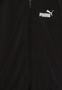 Svart zip-jacka tillverkad av ett mjukt, lättviktigt tyg. Har en vit Puma-logotyp på den övre vänstra bröstet. Materialet har en matt finish.