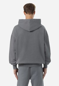 Übergroßer grauer Kapuzenpullover aus weichem Baumwollgemisch. Verfügt über eine große Kapuze, gerippte Bündchen und Saum. Einfaches Design ohne Muster oder Akzente.