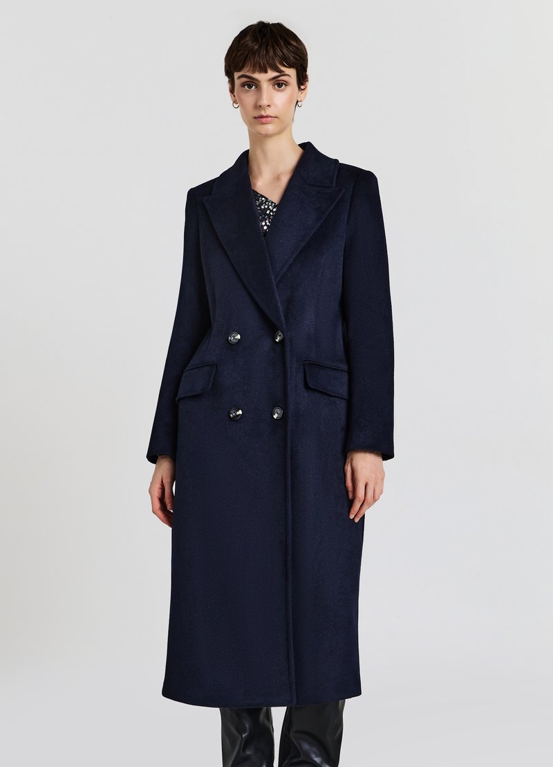 Lungo cappotto di lana blu navy con design doppiopetto, ampie alette, e tasche laterali, con texture liscia e bottoni lucidi.