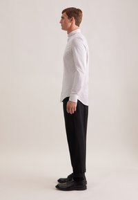 Wit geblokt overhemd met een knoopkraag, gecombineerd met zwarte, slim fit broek en zwarte nette schoenen, van de zijkant weergegeven.