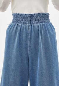 Ljust blå denimbyxor med resårmidja och breda ben. Tyget har en mjuk textur med minimala blekningar.