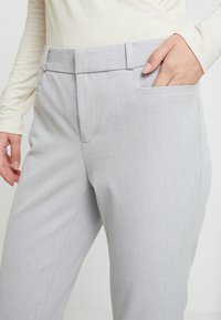Pantalones ajustados de color gris claro, confeccionados en un tejido suave, con cintura plana, trabillas y bolsillos laterales. Textura sutil en toda la tela.