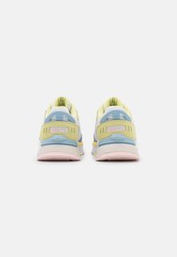 Puma löparskor med en vit och ljusgrå överdel, gula accenter, blå hälkappa och rosa sula. Nätstruktur för andningsförmåga.