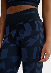 Marineblå leggings med ett geometriskt mönster i varierande nyanser av blått, med hög midja och ribbad textur. Märkt "hummel" vid midjan.