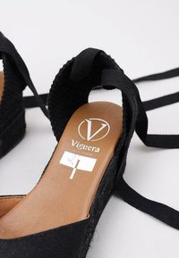 Alpargatas de cuña negras con parte superior de tela texturizada, cintas para atar y una plantilla de cuero natural con un logo.