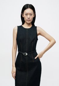 Ärmlös mörk jeansklänning med detaljer i orange söm och ett svart bälte med spänne i silver, figursydd passform och sidofickor.