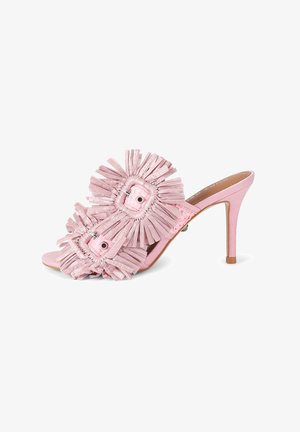 Roze muil sandaal met hoge hak, twee grote fringed bloemversieringen en een open teen op een witte achtergrond.