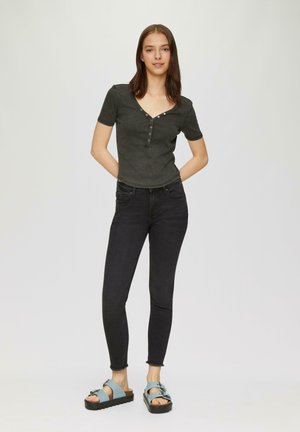Donkergrijze, aansluitende top met korte mouwen en een V-hals, voorzien van knoopdetails. Gecombineerd met zwarte skinny jeans en blauwe plateausandalen. Minimalistisch ontwerp.