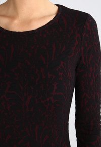 Czarna sukienka z burgundowym kwiatowym wzorem, teksturowany materiał oraz okrągły dekolt i długie rękawy.