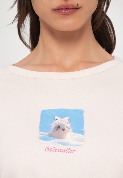 Hele-roosa puuvillane t-särk, millel on ruudukujuline graafika valgest jänesest roosa vibuga sinisel taustal. Tekstiks on "Holzweiler."