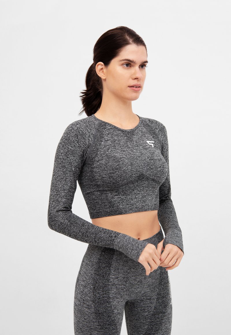 Woman in gray seamless long-sleeve crop top and matching high-waisted leggings, standing against a plain white background.