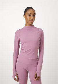 Langermet, tettsittende topp i myk rosa stoff med høy hals og tommelhull, kombinert med matchende høyt midje leggings.