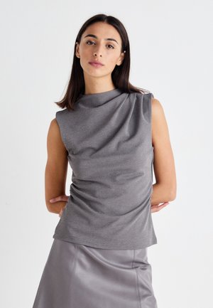 Top grigio senza maniche con design drappeggiato e dettagli lucidi sottili; abbinato a una gonna in pelle grigia liscia.