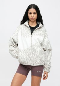 Ελαφρύ μπουφάν με φερμουάρ σε μπεζ χρώμα με διακριτικό σχέδιο ζώου, που διαθέτει όρθιο γιακά και ελαστικά μανίκια.