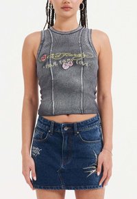 Šedý zkrácený top s vyšívaným nápisem "Odmítám svou lásku" a květinovými akcenty, spárovaný s modrou džínovou sukní s bílou výšivkou.