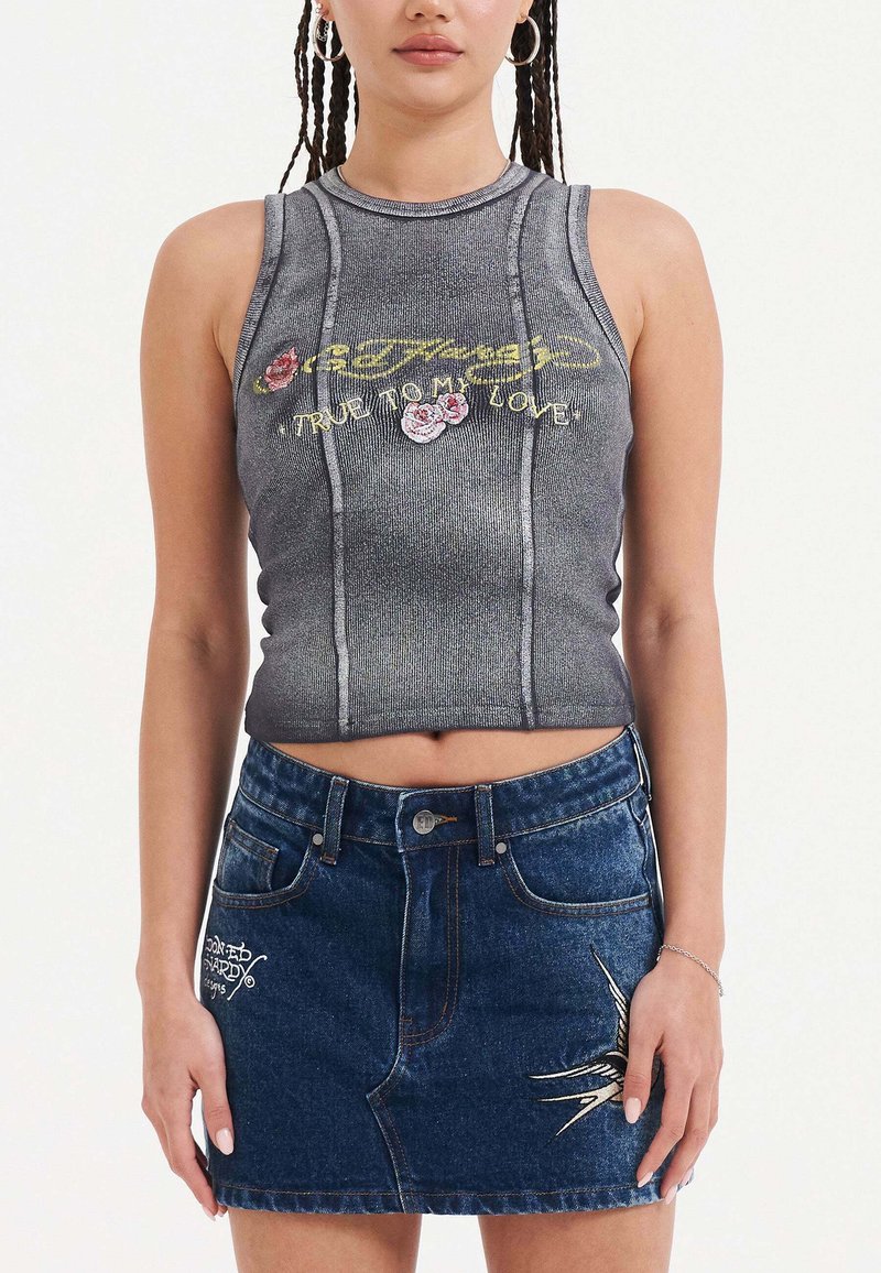 Šedý zkrácený top s vyšívaným nápisem "Odmítám svou lásku" a květinovými akcenty, spárovaný s modrou džínovou sukní s bílou výšivkou.