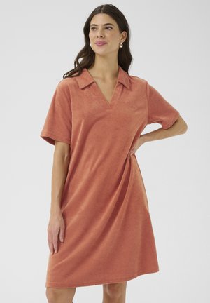 Terracotta polo jurk van zacht, textuurgegeven fabric met korte mouwen en een V-hals. Loose fit die net boven de knie valt. Subtiel logo-detail.