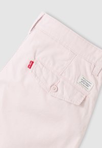 Τσέπη ροζ ανοιχτού χρώματος με πτυσσόμενο καπάκι με κουμπί, κόκκινη ετικέτα Levi's και ραμμένη ετικέτα μάρκας Levi Strauss πάνω από την τσέπη.