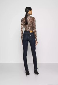 Maglione a maniche lunghe, fitted, con stampa leopardata; jeans in denim scuro con una targhetta in pelle color beige in vita e cuciture dorate, abbinati a tacchi neri.