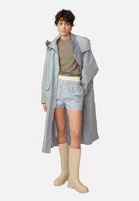 Hellblauer wasserdichter Mantel, graues Hemd, gestreifte Shorts und beigefarbene Gummistiefel. Einfaches Design mit kontrastierenden Farben und Texturen.