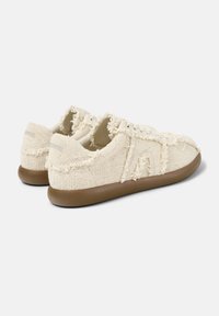 Sneaker beige realizzati in tessuto texturizzato con bordi sfilacciati, dotati di una suola in gomma marrone e dettagli di cucitura sottili.