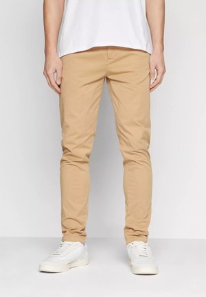 Chinos khaki con vestibilità slim, realizzati in cotone. Presentano una superficie liscia, passanti per la cintura e tasche, abbinati a sneakers bianche.