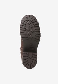 Hnědá kožená podrážka boty s hlubokým vzorem a kruhovým logem. Texturovaná guma poskytuje přilnavost; tvar se přizpůsobuje noze pro podporu.