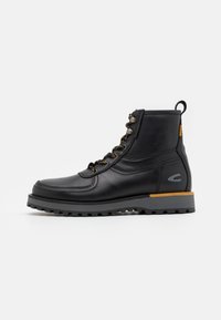 Black leather boot with a rounded toe, featuring metallic eyelets and orange accent on the heel. Textured rubber sole for grip.