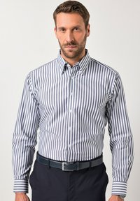 Camisa de botón con finas rayas verticales en azul y blanco, diseño con cuello, mangas largas y corte clásico. Combinada con un cinturón oscuro.