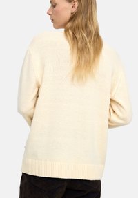 Sweter w kolorze kremowym, wykonany na drutach, o luźnym kroju, z prążkowanym wykończeniem i subtelną teksturą. Posiada obniżone ramiona i długie rękawy.